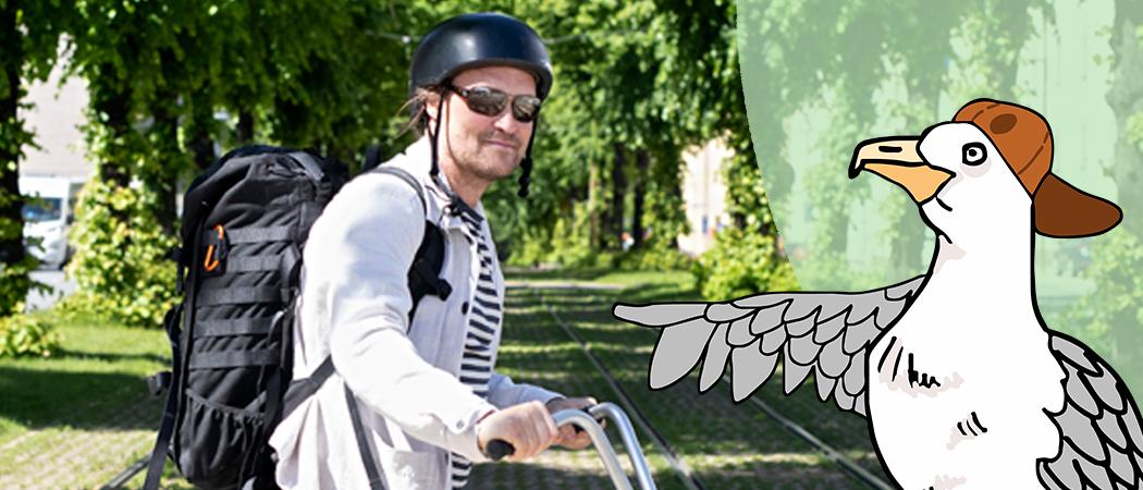 Mies reppu selässä, musta kypärä päässä, taluttaa pyörää raitiokiskojen yli puistomaisessa kaupunkimaisemassa. Piirretty lokki lätsä päässä osoittaa siivellään miestä.