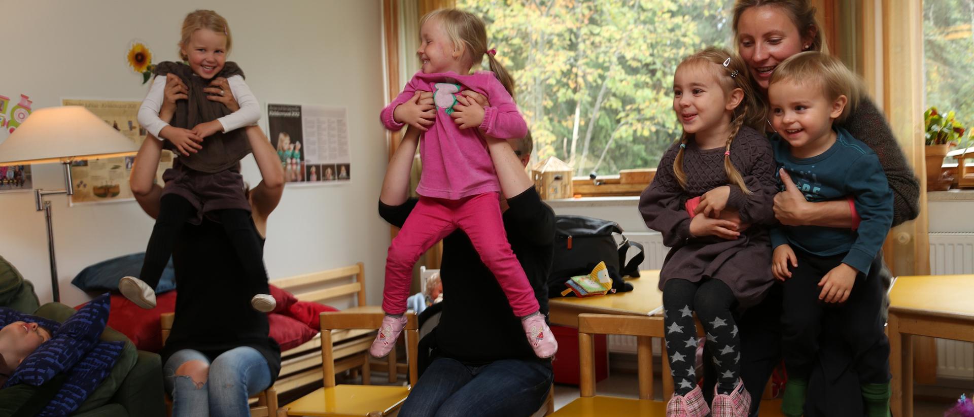 Vanhemmat seisovat piirissä ja nostavat lapsia sylissään