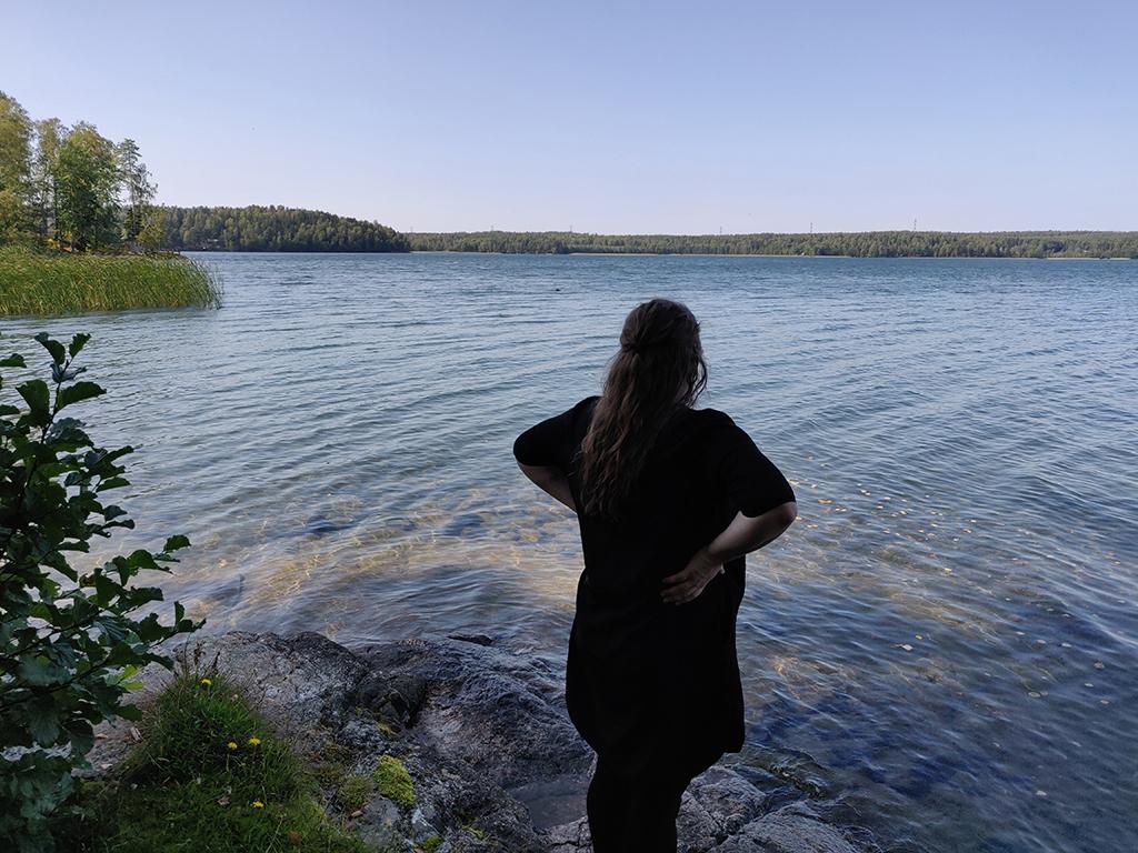 nainen selin rannalla katselemassa järven ulapalle kesällä