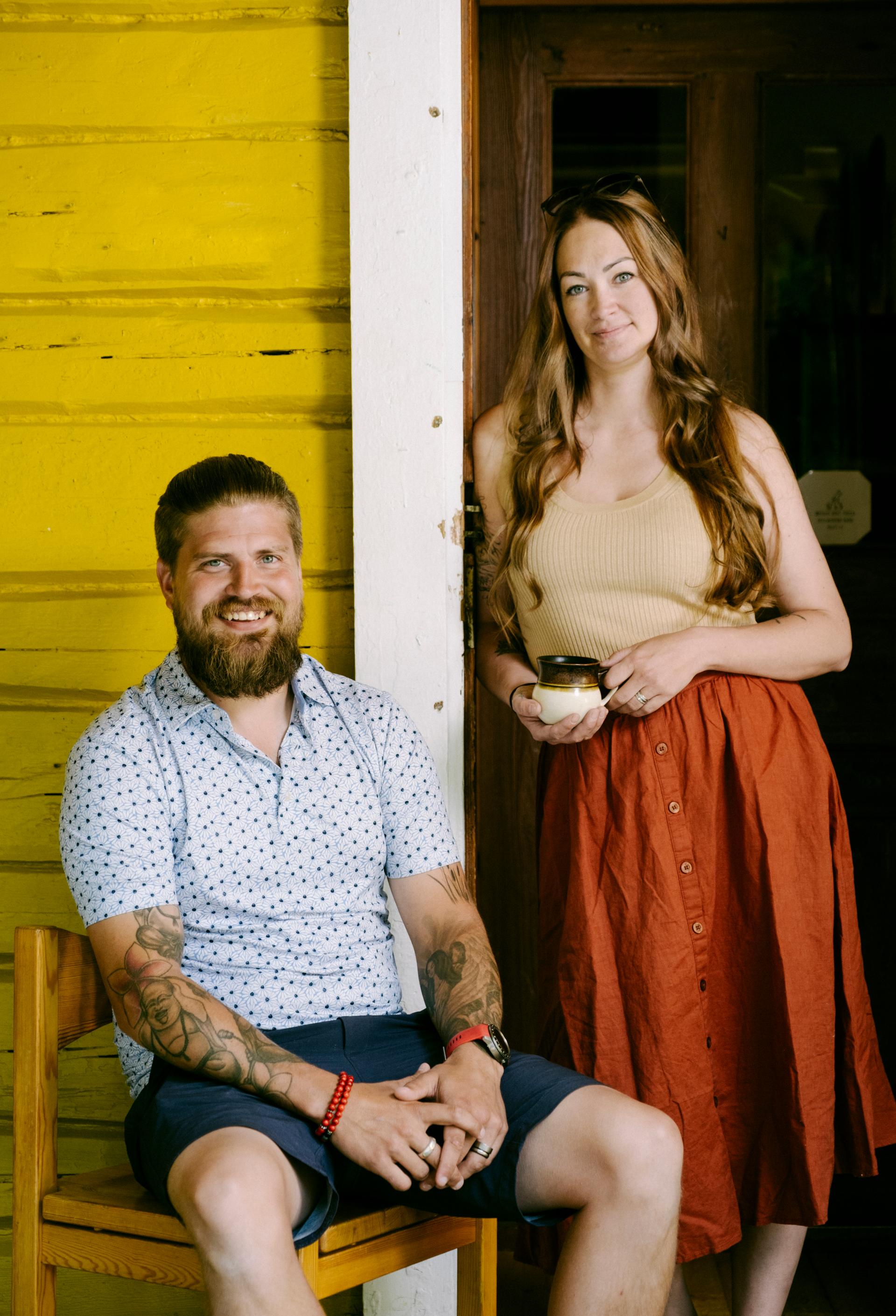 Mies istuu tuolilla, vieressä seisoo nainen kahvikuppi kädessä.