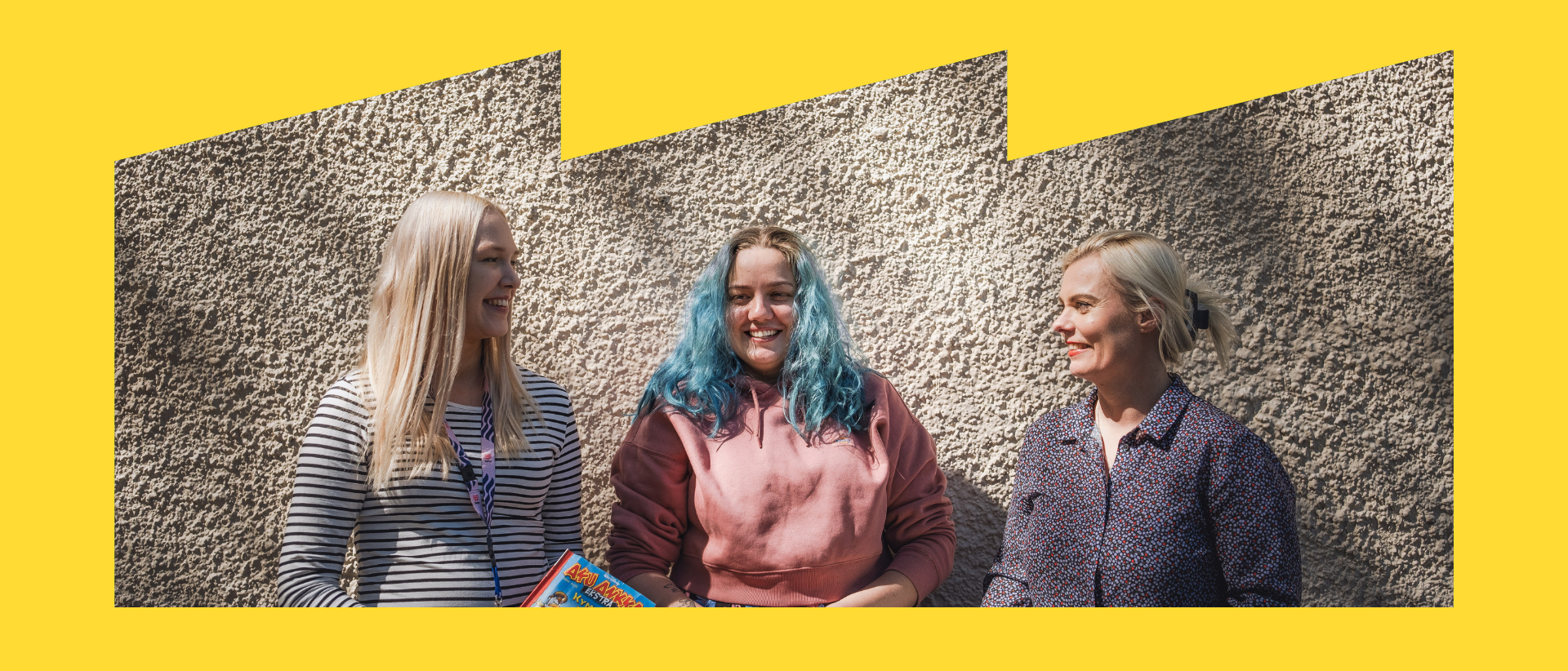 kolme henkilöä koulun seinää vasten Oulunkylän yhteiskoululla