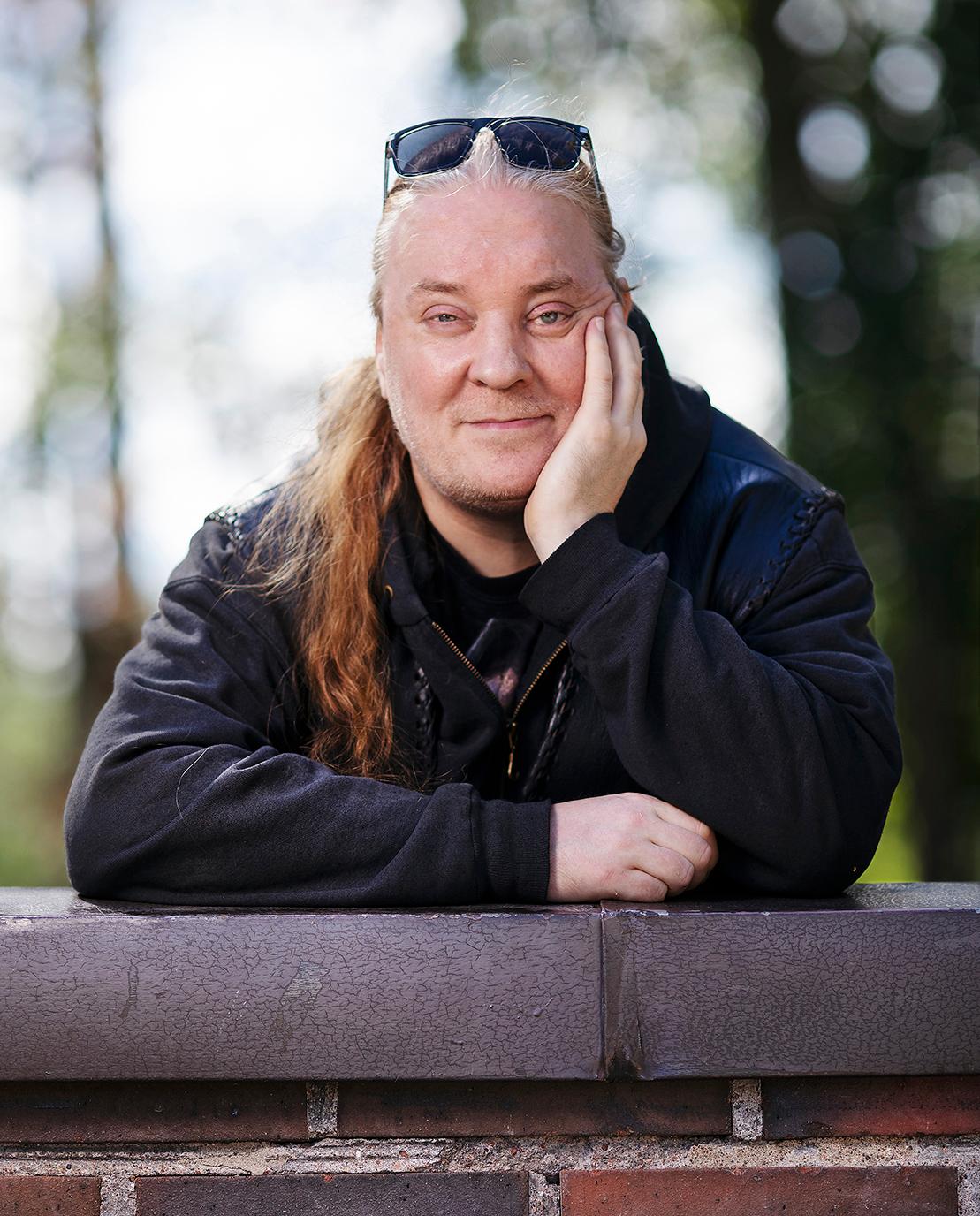 Mustiin pukeutunut pitkähiuksinen vapaaehtoistyöntekijä Jan nojaa käsiinsä Oulunkylän kirkon takapihan muuria vasten.