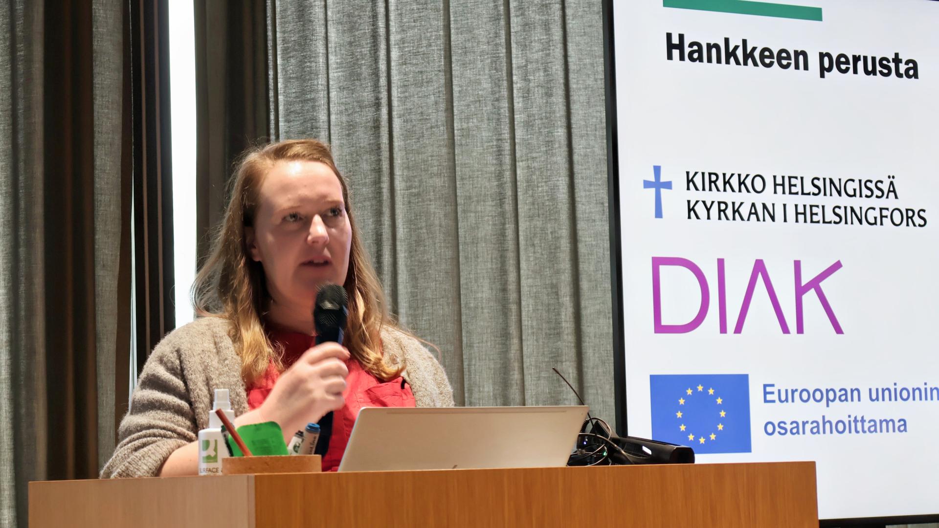 Nainen puhuu mikrofoniin puhujakorokkeella