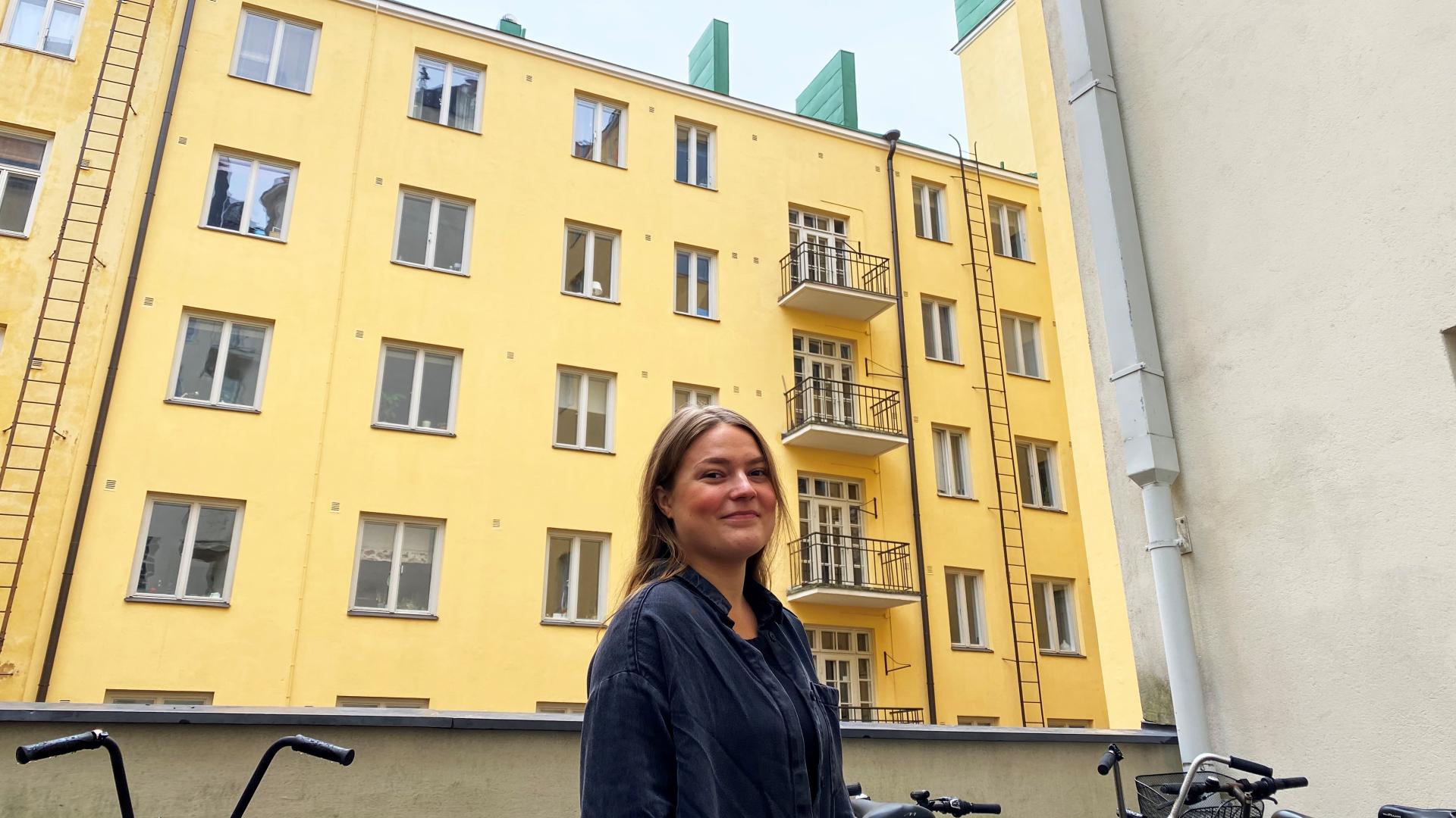 En leende kvinna, i bakgrunden ett gult höghus.