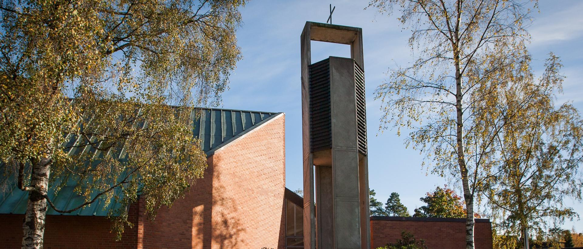 Punatiilinen kirkko ja betoninen kellotapuli syysmaisemassa