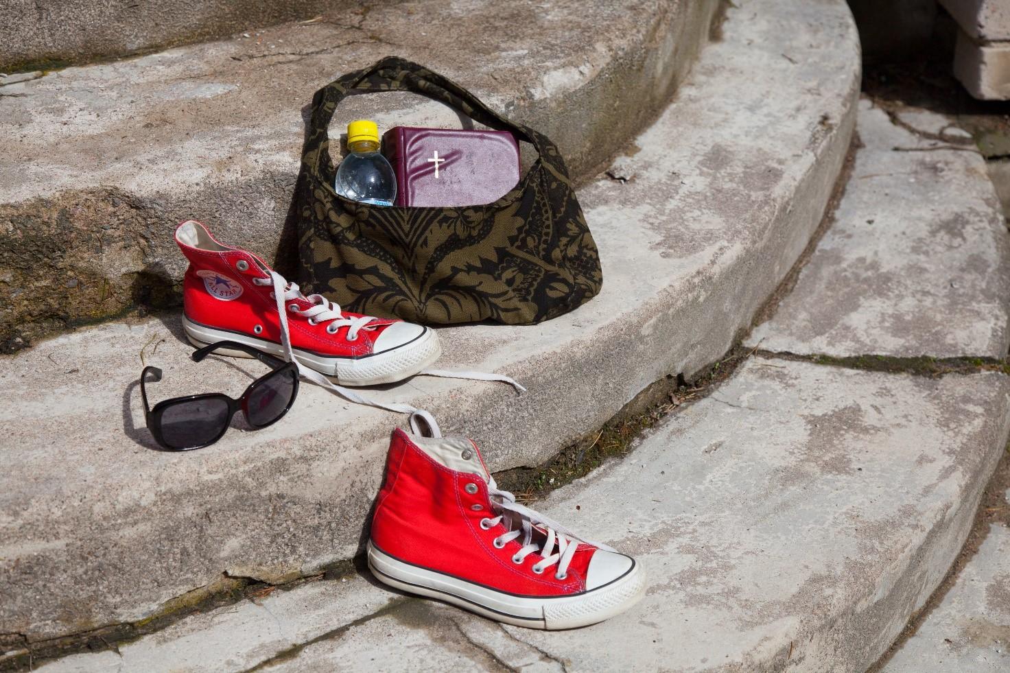 kirkon portailla aurinkolasit, punaiset tennarit ja kassi, josta pilkottaa Raamattu