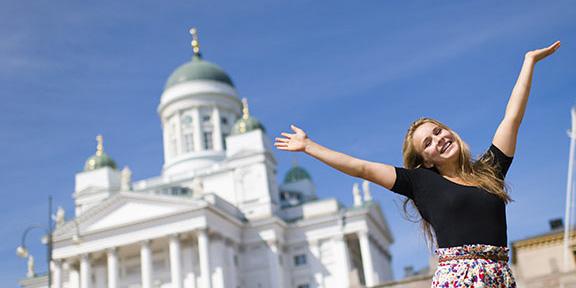 Kuvassa Helsingin tuomiokirkko ja sen edessä iloinen tyttö kädet ylhäällä