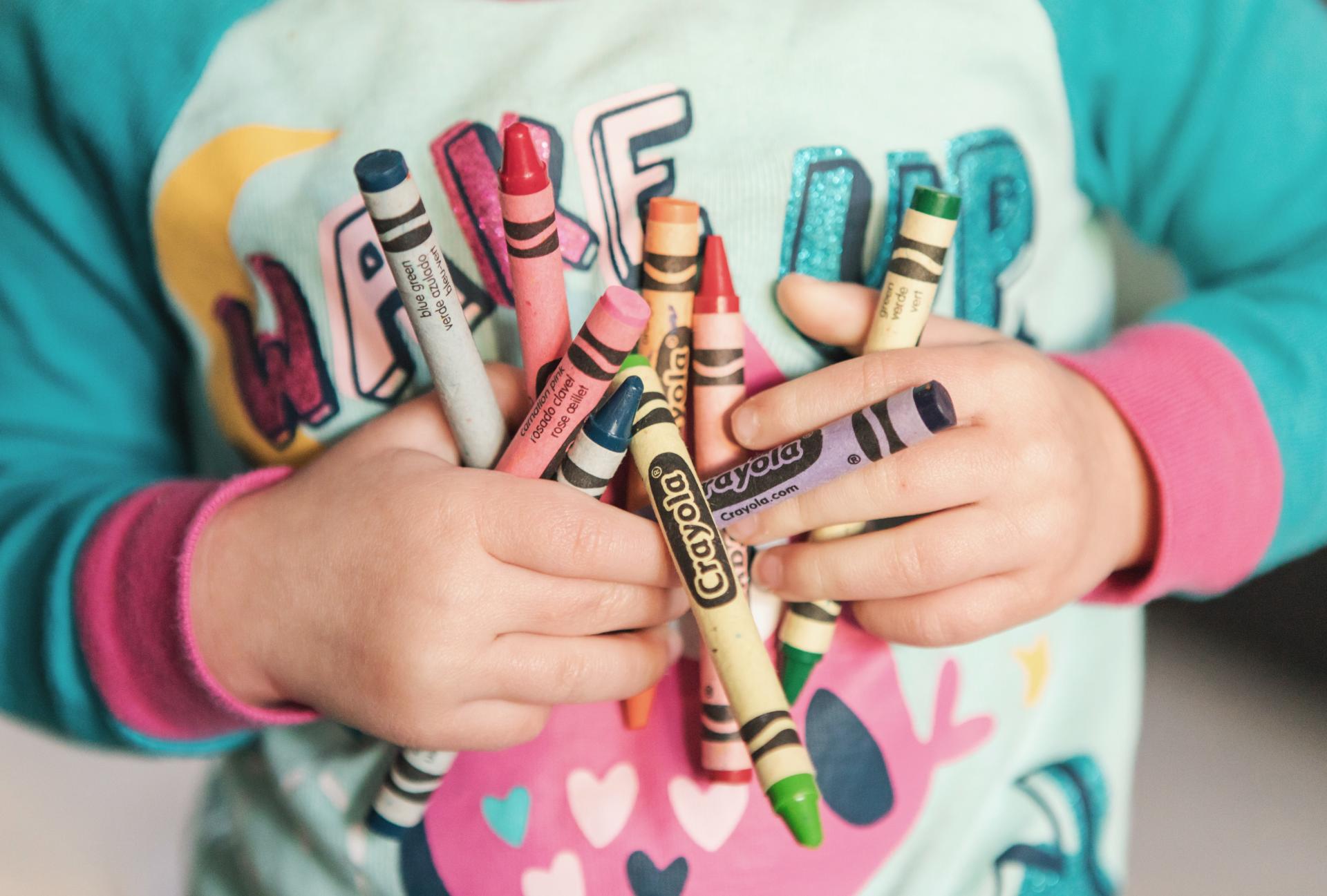 Ett barn som håller i färgpennor av olika pennor.