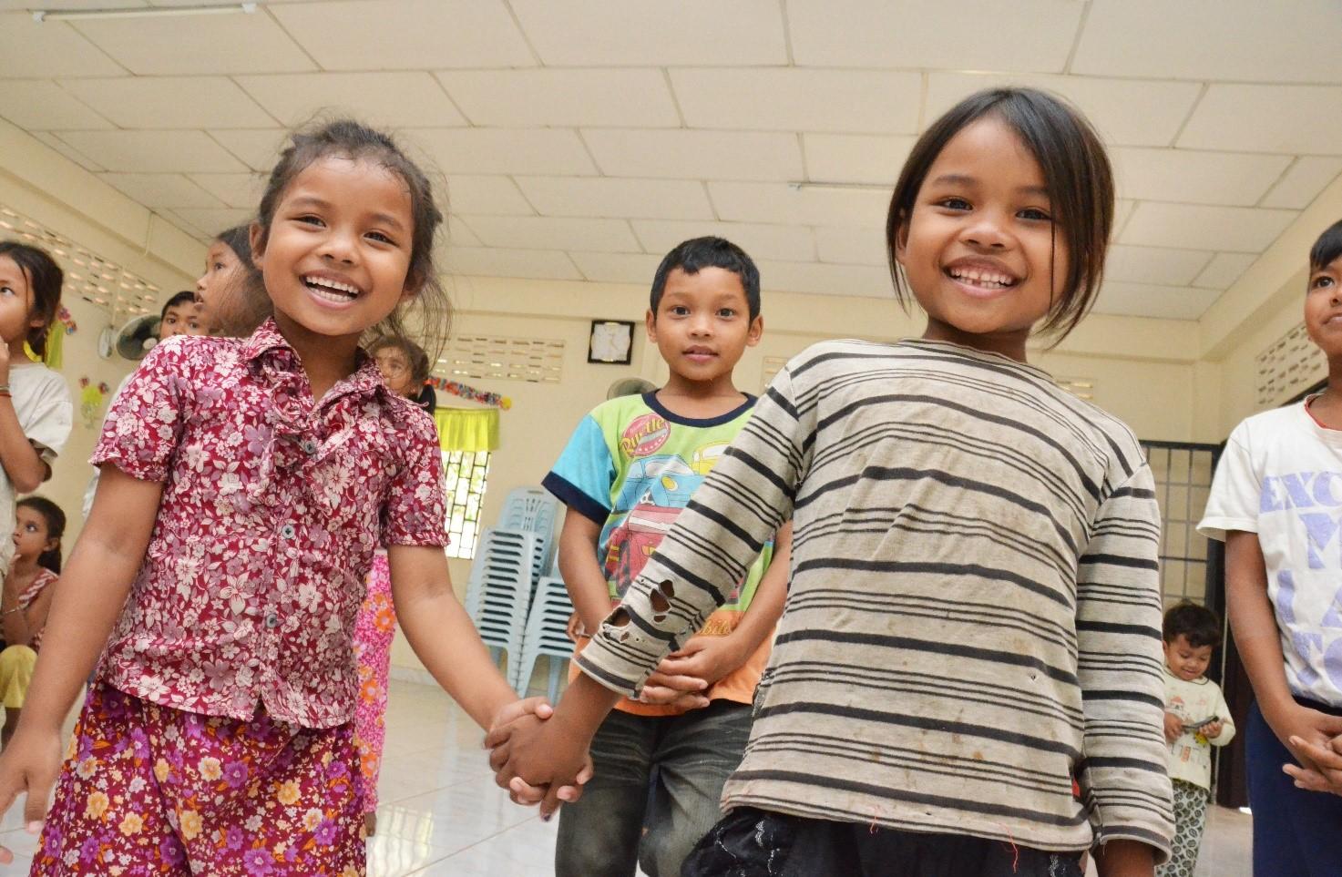 Hymyilevät thaimaalaiset lapset käsi kädessä salissa