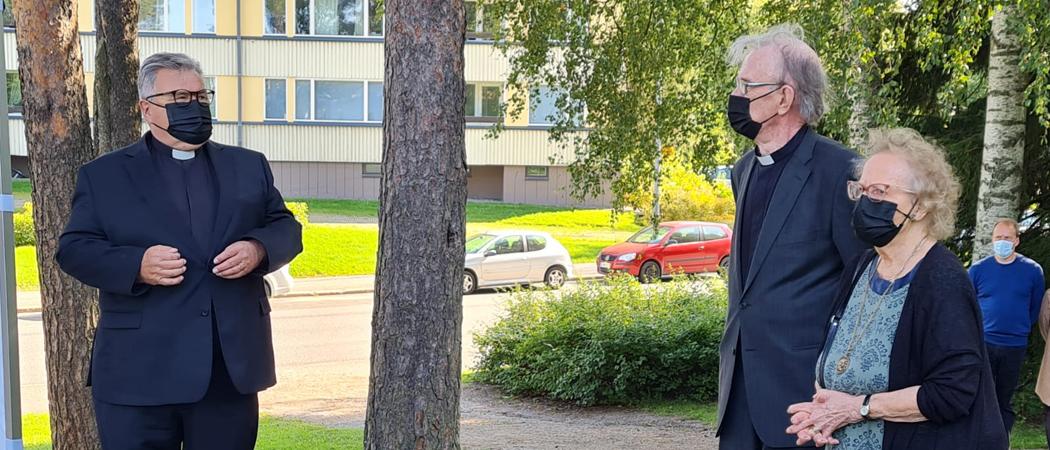 Kannelmäen kirkon pihalla kesäisessä säässä rovasti Pentti Simojoki rouvineen pitää puhetta kirkkoherra Sakari Enroldille.