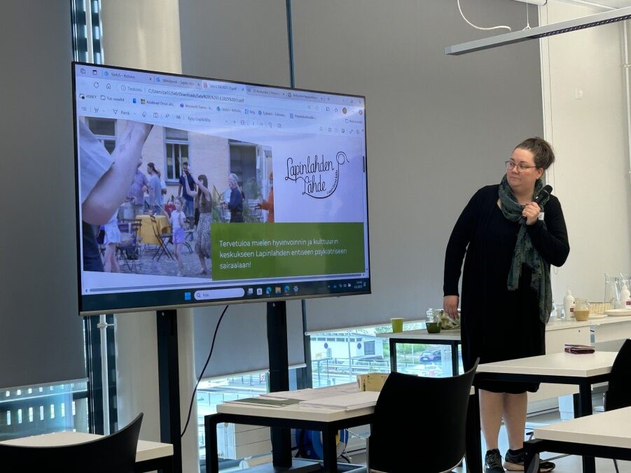 Isolla näytöllä diaesitys, jota pitää oikealla seisova puhuja