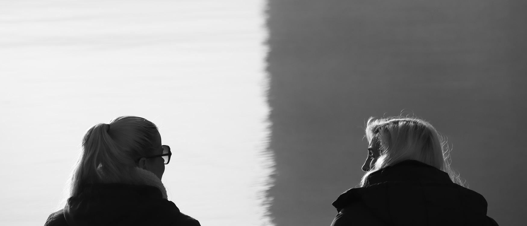 mustavalkoisessa valokuvassa kaksi naista juttelemassa ulkona veden äärellä selin kameraan.