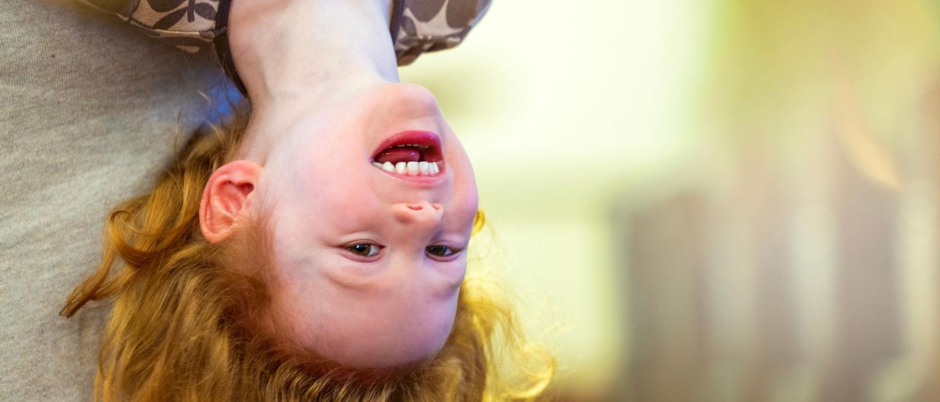 Kiharatukkainen lapsi roikkuu pää alaspäin