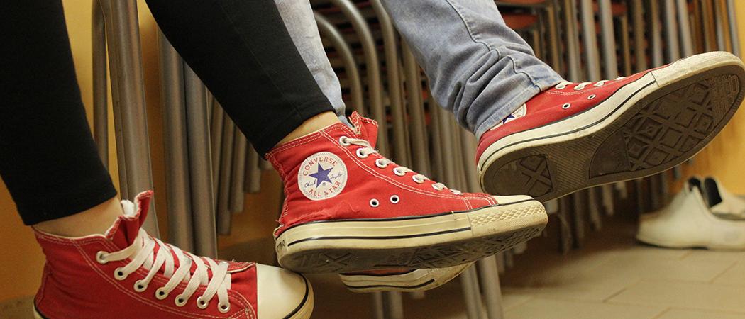 Tuolipinojen päällä istuu kaksi nuorta joiden jalat näkyvät kuvassa. Molemmilla jalassa punaiset converse tennarit.