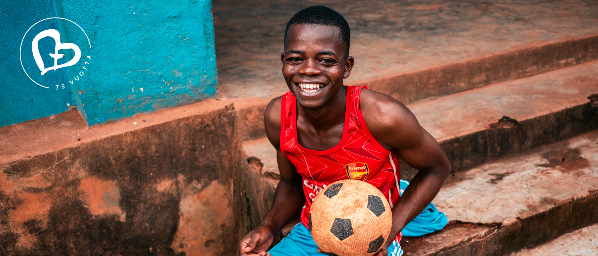 Nuori hymyilevä poika kädessään jalkapallo