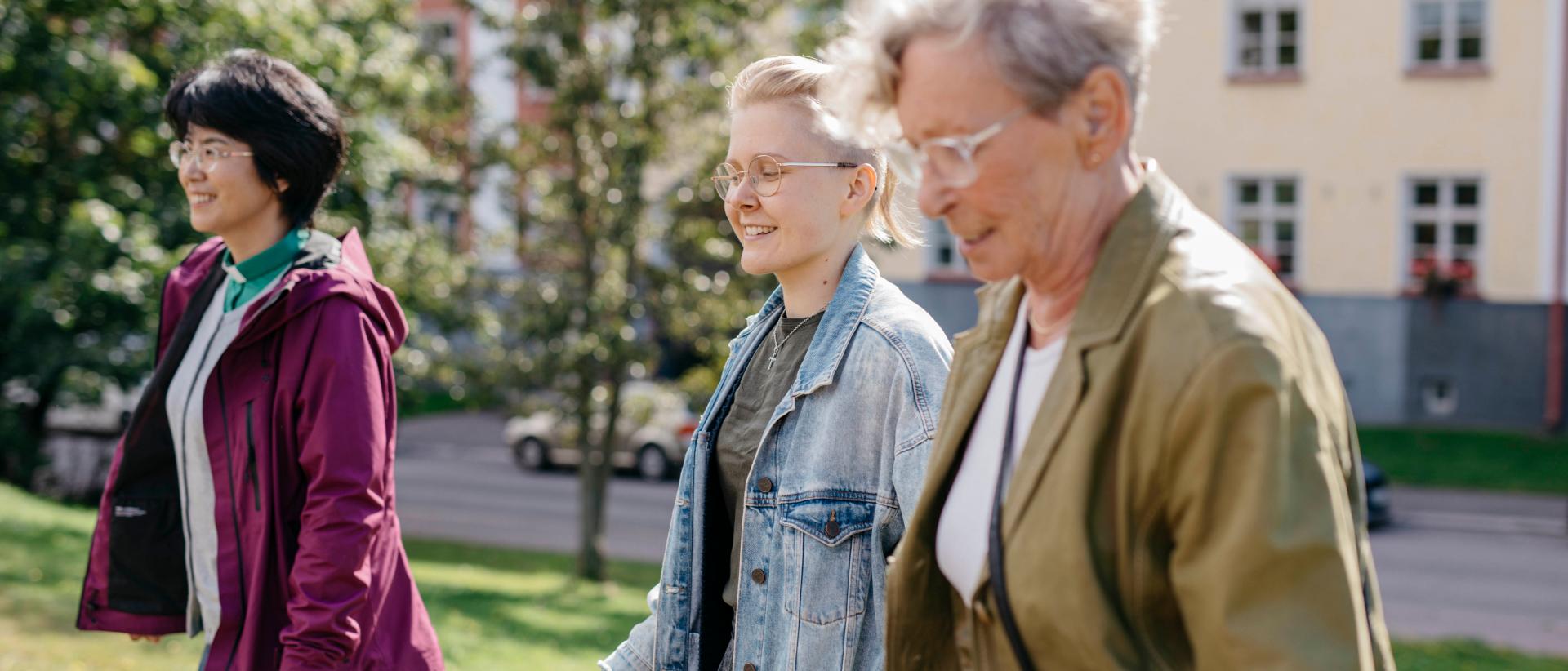 Diakoniatyöntekijä kävelee kahden naisen kanssa, taustalla puisto