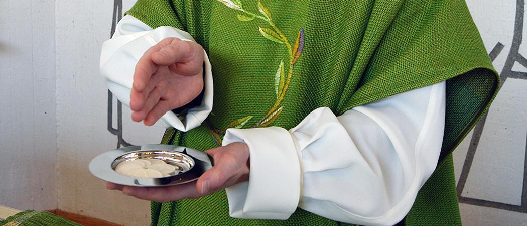 Vuosaaren kirkon alttarilla pappi kädessään ehtoollisleivät.