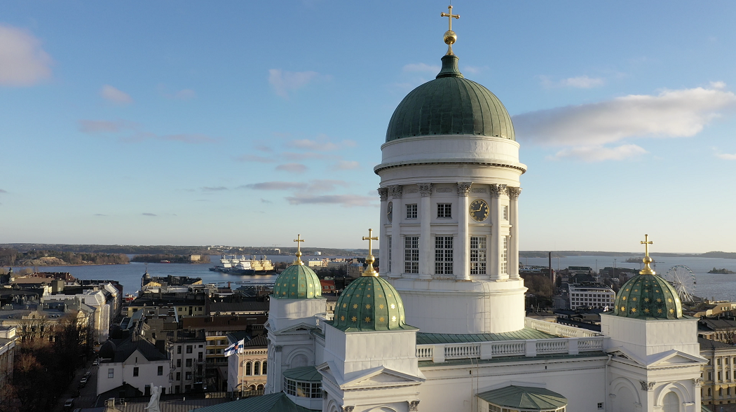 Helsingin tuomiokirkko kokonaisuudessaan, taustalla sinistä taivasta ja kaupunkimaisemaa.