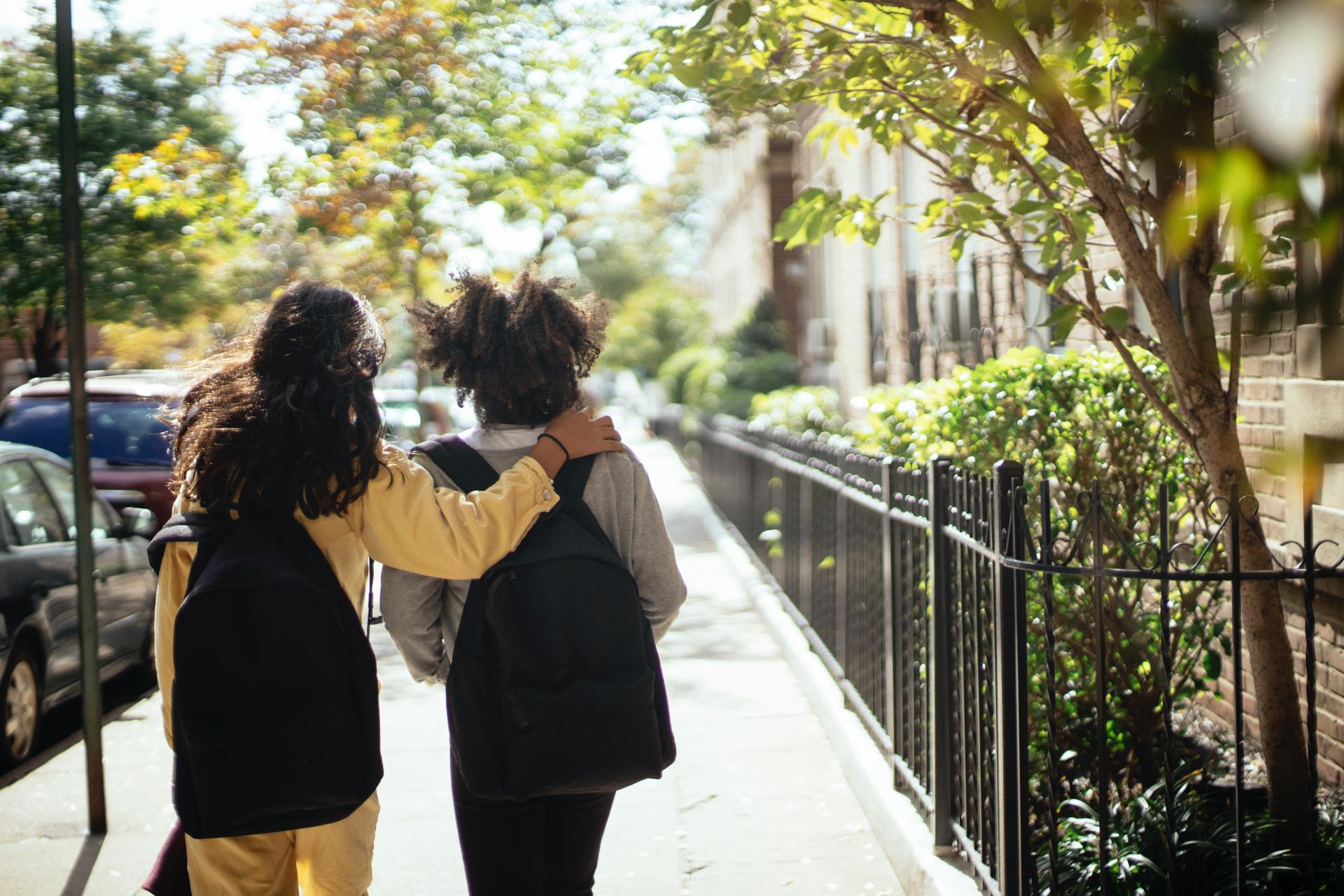 Kaksi reppuselkäistä tyttöä kävelee kadulla selät kameraan päin.