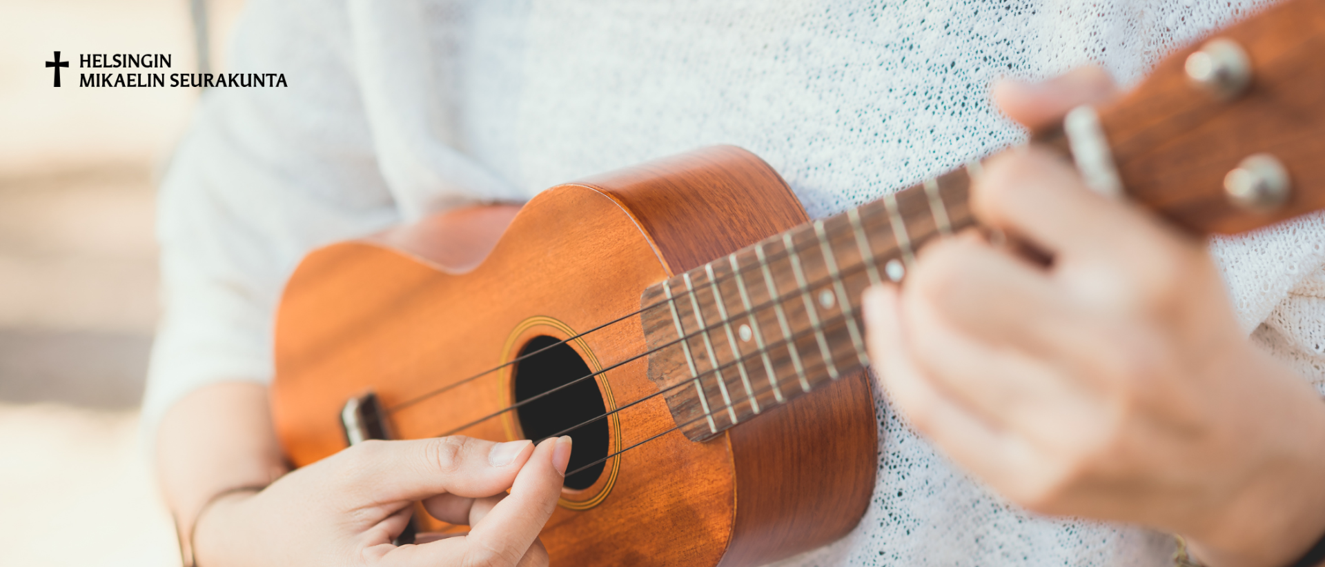 henkilö soittaa ukuleleä, helsingin mikaelin seurakunnna logo