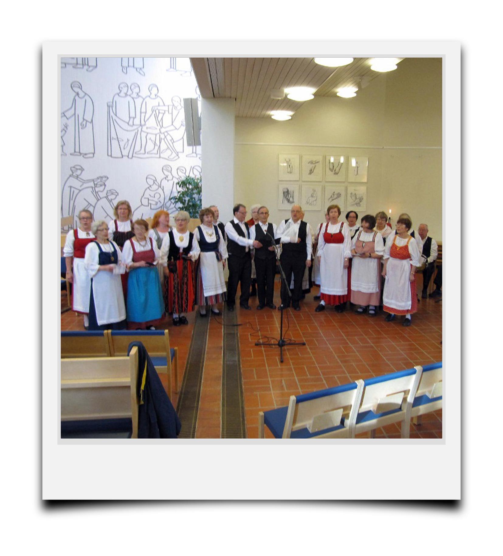 Polaroid kuvassa Vuosaaren kirkossa Sakarat Laulupelimannit esiintymässä, ihmisiä kansallispuvuissa.