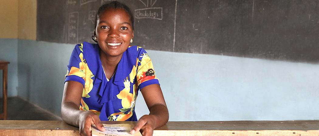 Afrikkalainen nuori nainen kirja kädessään hymyilee.