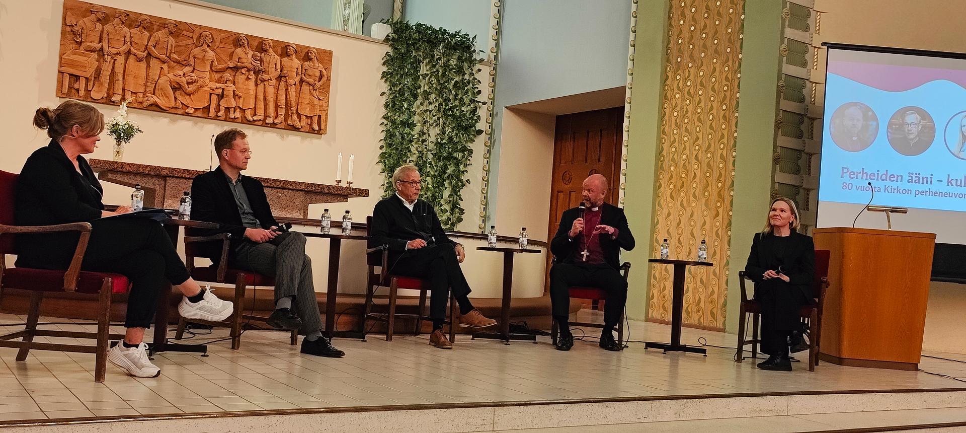 Viisi keskustelijaa istuu puolikaaressa, taustallaan Kallion kirkon alttari