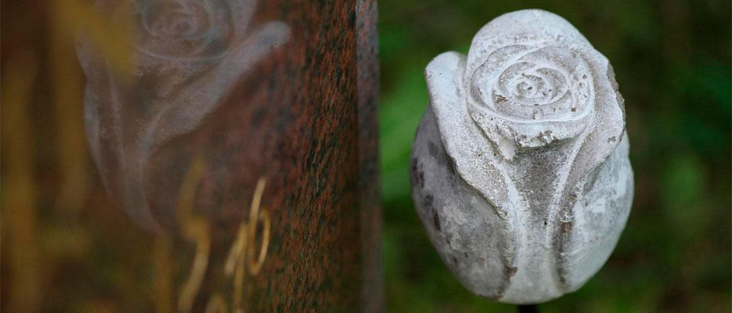 Kuvassa osoittain näkyvä punagraniittikivinen hautakivi ja valkoinen kiviruusu