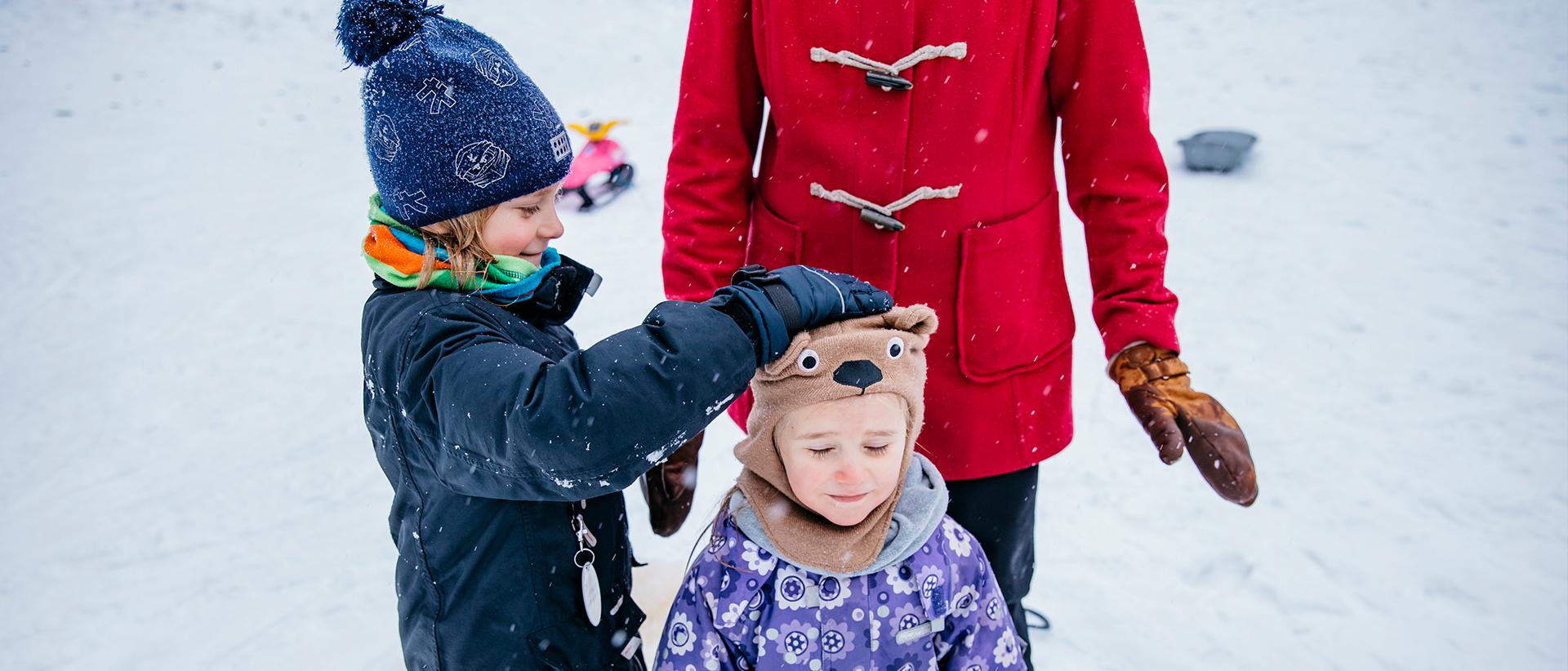 Kaksi lasta talvitamineissa taustalla punatakkinen aikuinen. Kuva: Elina Manninen_Keksi