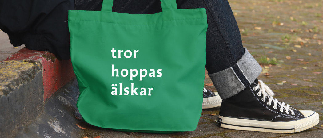 En tygkasse med orden tror, hoppas, älskar i vit text på grönt botten.