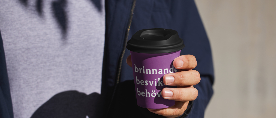 En person håller en kaffemugg med texten brinnande, besviken, behövd i vitt på lila botten.