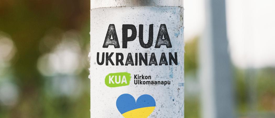 Kadulla olevassa tolpassa liimattu lappu, jossa lukeea Apua Ukrainaan, sekä Kirkon Ulkomaanavun logo.