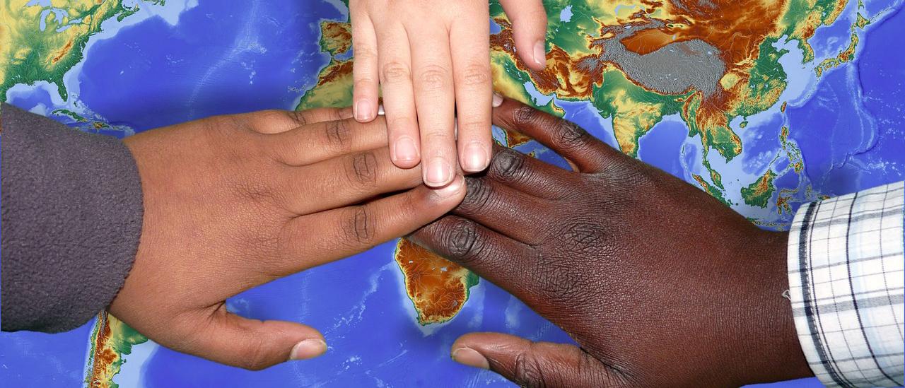 Kolmeen eri etniseen ryhmään kuuluvien ihmisten kädet päällekkäin kartan päällä
