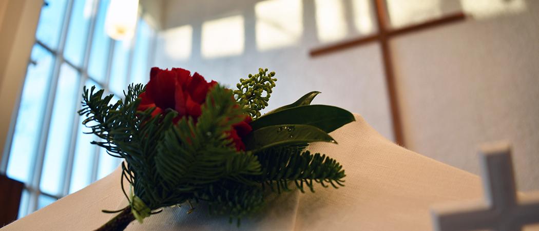 Lähikuvassa kukka arkun päällä kirkossa, taustalla näkyy risti.