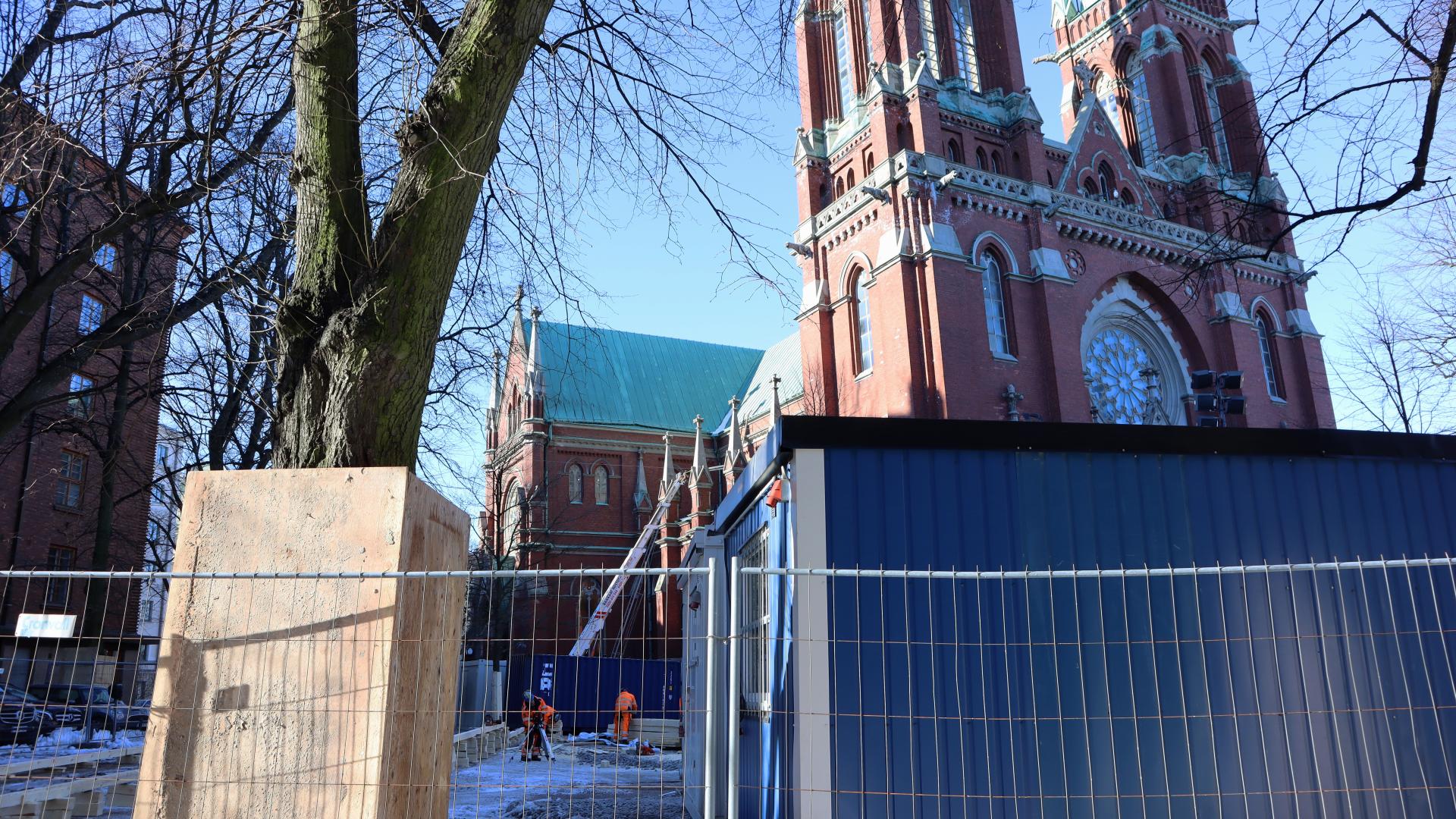 Ett staket runt byggkontainrar och en stor kyrka