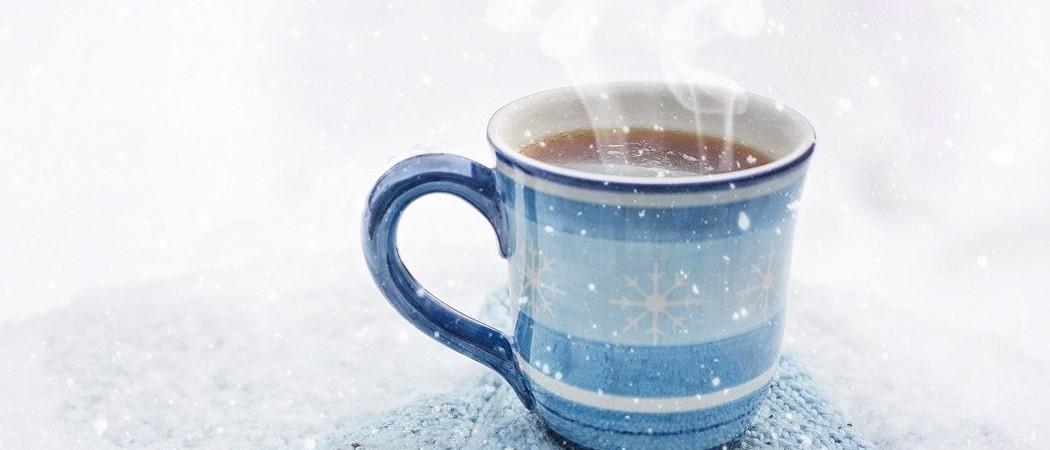 Kahvikuppi, jossa kuuma kahvi höyryää. Ympärillä sataa lumihiutaleita