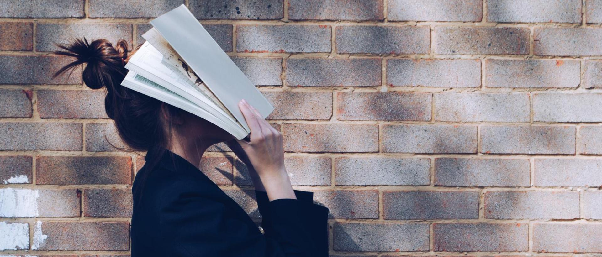 En person står med en bok öppnad rakt i ansiktet.