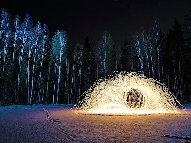 Kari Hiltusen valokuvassa Tulipesä on tummalla lumisella metsäaukiolla renkaita jonossa, jotka näyttävät palavan kuin tähtisädetikut ja muodostavan 