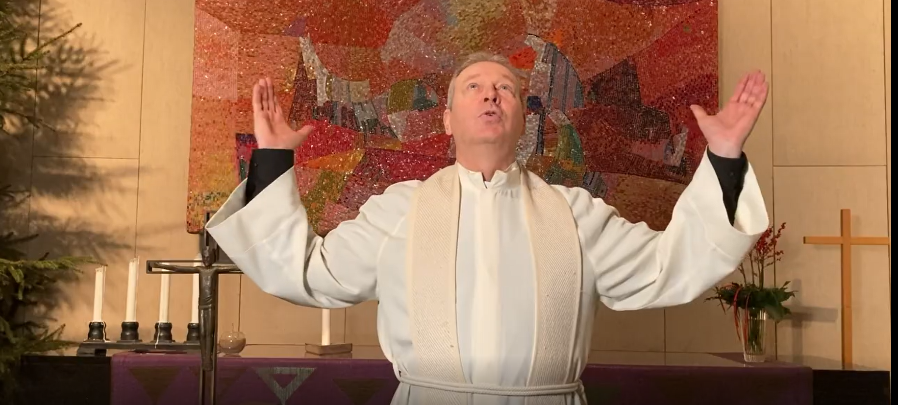 Taneli Hassinen Munkkivuoren kirkon alttarin edessä valkoisessa albassa kädet kohotettuna ylös ja  katse kohotettuna ylös