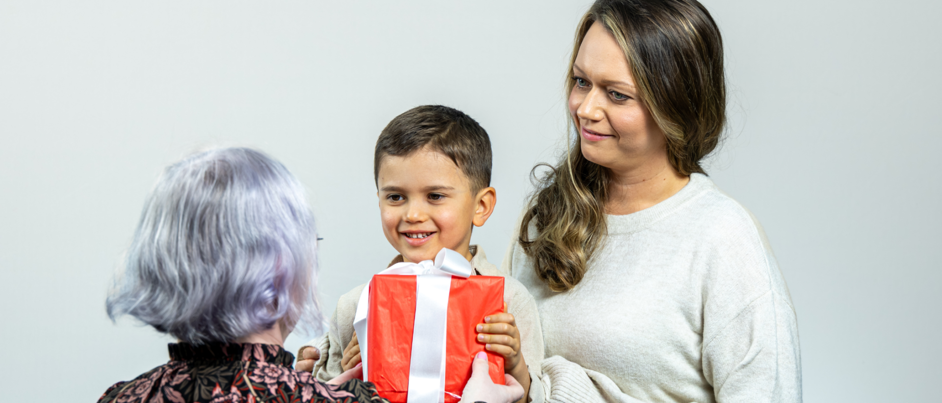 Nainen ojentaa lahjapaketin pikkupojalle, joka on &auml;itins&auml; syliss&auml;.