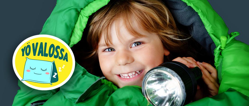 Vihreässä makuupussissa iloinen lapsi taskulampun kanssa.