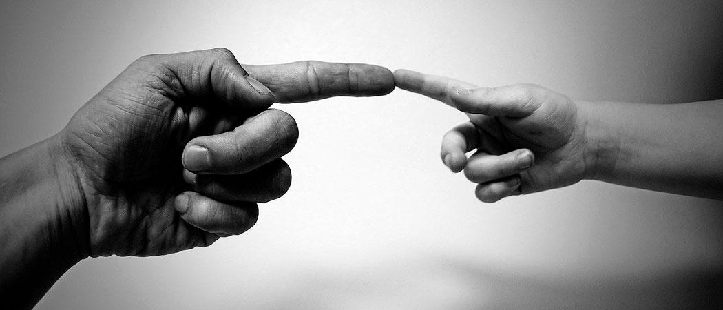 Mustavalkokuvassa miehen etusormi koskettaa lapsen etusormea