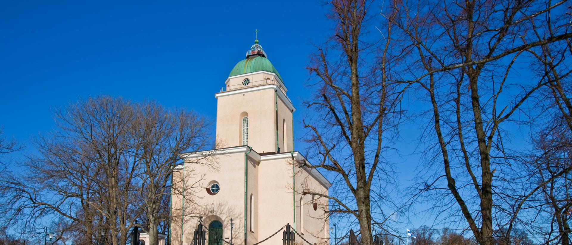 Suomenlinnan kirkko lehdettömien puiden keskellä, kirkkaansininen talvinen taivas taustalla.