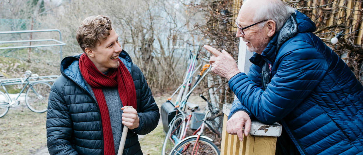 Nuori poika juttelee iloisesti vanhemman herran kanssa pihalla. Takana polkupyöriä. Kuva: Elina Manninen/Keksi