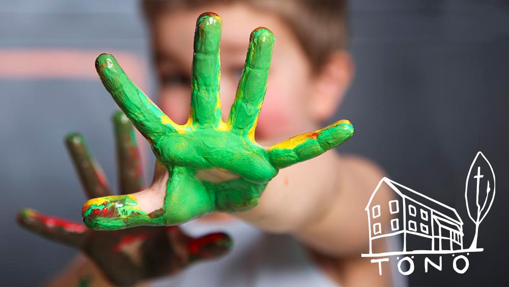 Lapsi jonka kädet ovat vihreässä maalissa kurottaa kohti kameraa. Oikeassa alalaidassa Tönö-logo.