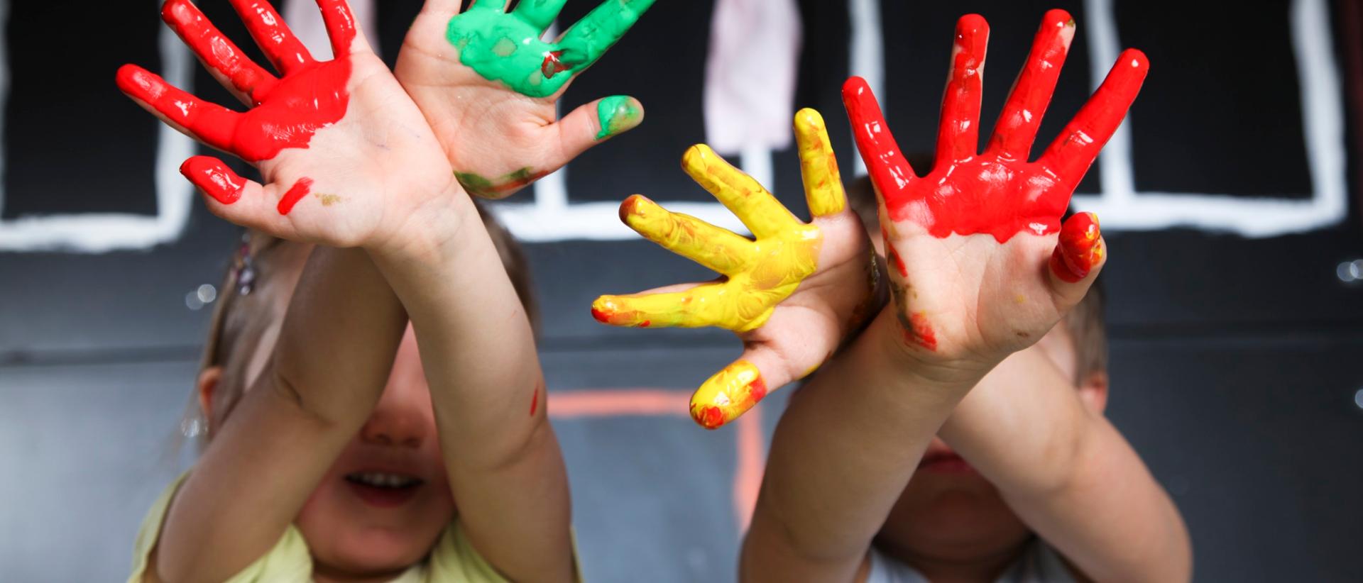 Kaksi lasta, etualalla lasten värikkäät sormiväreillä maalatut kädet