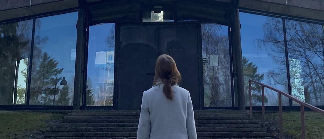 Nainen seisoo selin kameraan portailla Kannelmäen kirkon pääoven edessä.