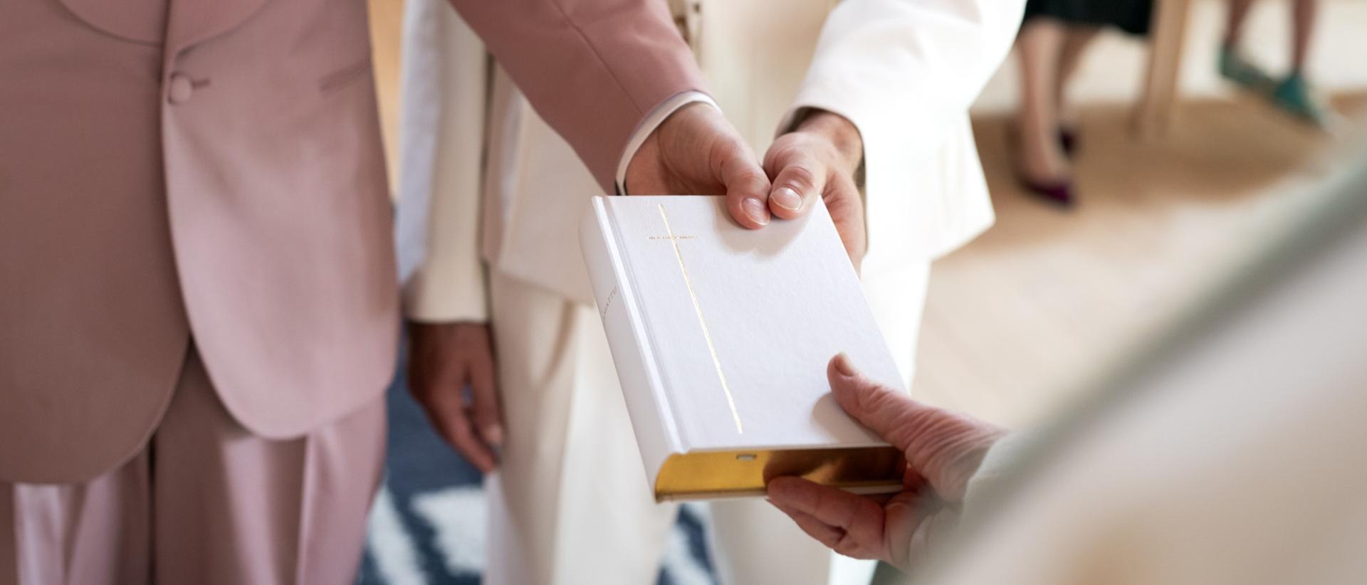 Lähikuva jossa pappi ojentaa vihkiraamatun kahdelle henkilölle