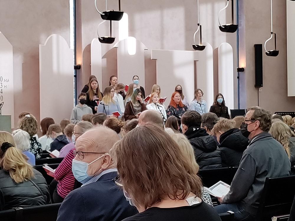 Ihmisiä  Mikaelinkirkossa messussa takaapäin kuvattuna taustalla nuorten kuoro