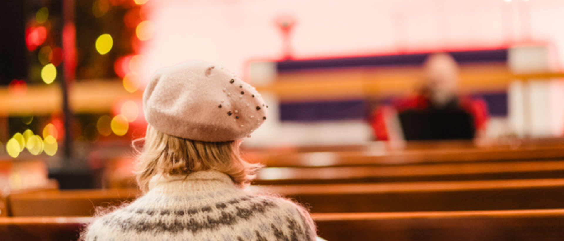 Nainen istuu jouluna kirkon penkissä, yllään vaaleanruskea villapaita ja baskeri